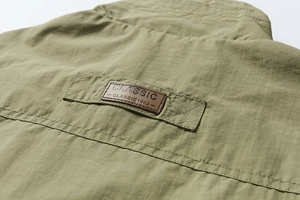 Détail d'un gilet extérieur vert armée montrant un patch en cuir et une texture quadrillée