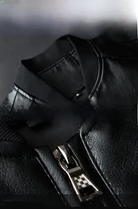 Detail of black leather jacket showing ribbed stand collar and checkered metal zipper