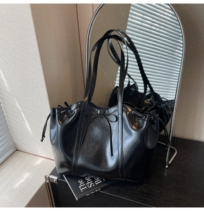 Detail of a black glossy tote bag with drawstring closure and bow decoration