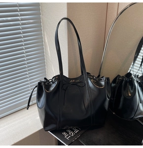 Detail of black glossy tote bag with bow accent and side drawstring design