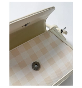 Detail view of the metal magnetic clasp and interior of the beige plaid crossbody bag