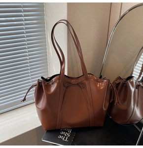 Detail of glossy brown tote bag featuring decorative bow and drawstring accents