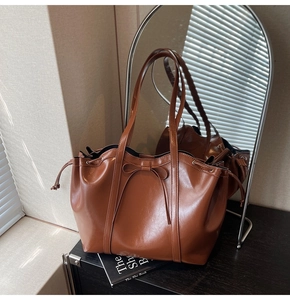 Detail of glossy brown tote bag featuring decorative bow and side drawstring closure