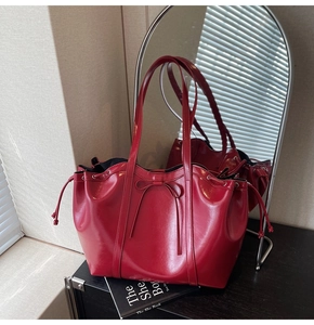 Detail of a red patent leather tote bag featuring a bow accent and drawstring sides