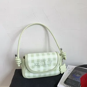 Detail of green plaid shoulder bag featuring cute cartoon embroidery and floral pendant