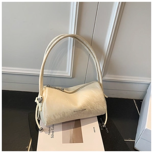 Detail of cream pleated cylinder bag featuring metal zipper and drawstring ball ornament