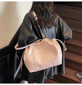 Pink glossy leather bucket bag with bow detail and drawstring shown as a shoulder bag