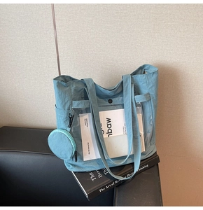Detail of light blue nylon tote bag featuring clear pocket and side coin purse