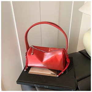 Detailed macro view of a red patent leather cylinder bag with silver zipper and metal ball charm
