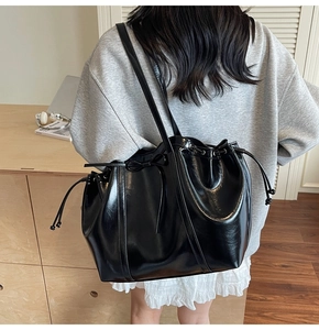 Detail of black glossy leather tote bag showing side bow tie and drawstring closure