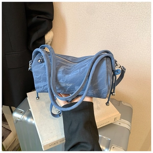 Detail view of blue barrel bag featuring ruched leather texture and side drawstring charm
