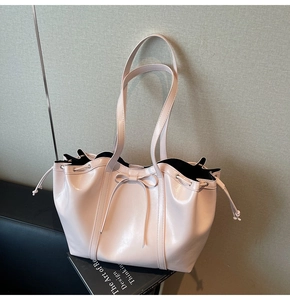 Pink patent leather tote bag with bow detail resting on a design book background