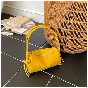 Detail of a yellow cylindrical pillow bag with glossy texture and silver metal ball accents