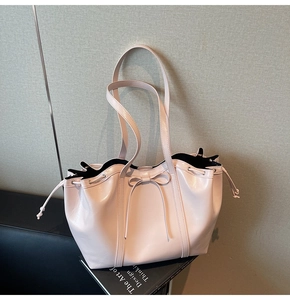 Detail showing the glossy pale pink tote bag with a bow decoration and drawstring closure