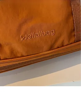 Gros plan du logo Wellaibag brodé sur le tissu en nylon marron du grand sac de voyage