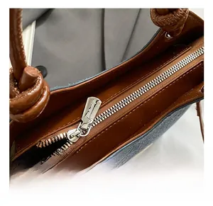 Détail du sac seau en jean contrasté avec fermeture éclair et poignée en cuir nouée