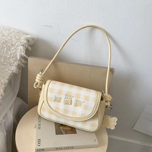 Macro shot of yellow plaid pattern with bread embroidery and biscuit charm on crossbody bag