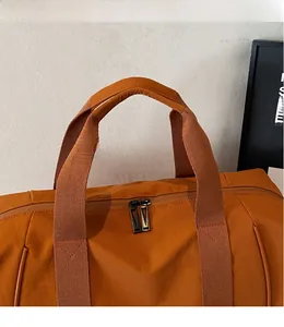 Détail du sac de voyage orange avec poignées tissées et double fermeture éclair en métal