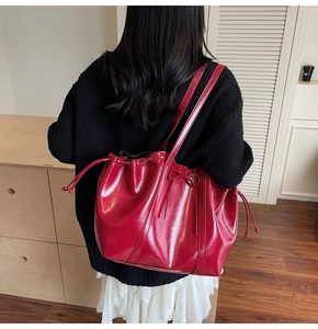 Detailed view of glossy dark red leather tote bag with drawstring and bow on black outfit