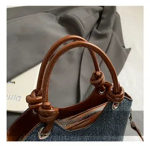 Détail du sac seau en denim bleu avec anse en cuir marron noué et finitions métalliques