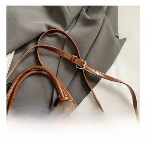Détail de la bandoulière en cuir marron réglable avec boucle argentée sur sac en jean