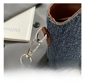 Vue détaillée du crochet en métal argenté et de la bandoulière en cuir du sac en denim
