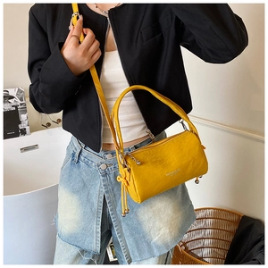 Detail of a bright yellow leather cylindrical crossbody bag with dual straps worn by model