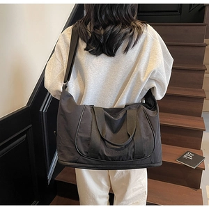 Modèle portant un grand sac de voyage noir en nylon avec bandoulière au style minimaliste