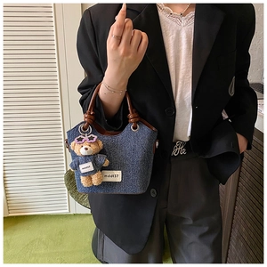 Détail du sac seau en jean avec poignée en cuir marron nouée et breloque ourson