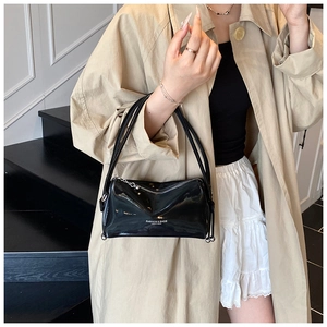 Detail of a black patent leather cylindrical handbag with silver hardware on a shoulder strap