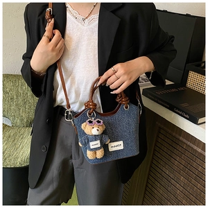 Détail d'un sac seau en denim avec bandoulière en cuir et charm d'ours en peluche mignon