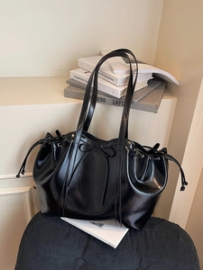 Minimalist black shiny leather tote bag with drawstring and bow detail on a velvet seat