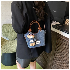 Mini sac seau en jean bleu avec poignées en cuir marron et breloque ours porté par mannequin