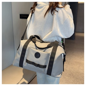 Rear view of model carrying a large grey travel bag with shoulder strap in a hallway