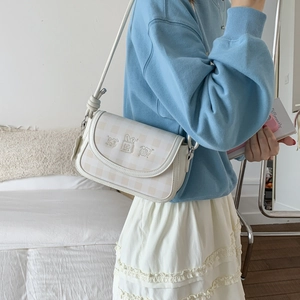 Detail of checkered saddle bag featuring cute cartoon embroidery and slim shoulder strap