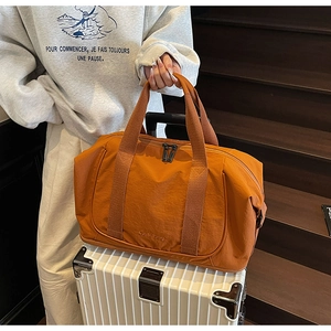 Vue détaillée d'un sac de voyage orange posé sur une valise blanche dans un cadre de vie