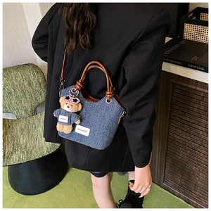 Détail du sac seau en denim bleu avec anses en cuir marron et pendentif en ours
