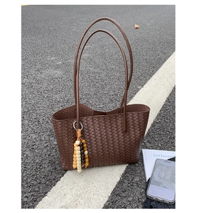 Close-up of a large dark brown woven tote bag featuring a colorful beaded tassel charm