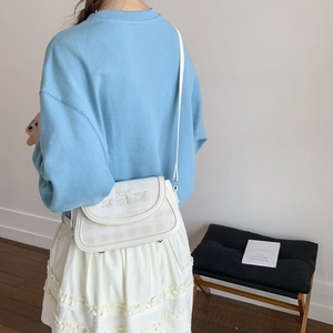 Cream crossbody bag with plaid flap and bread print worn by a model in casual outfit