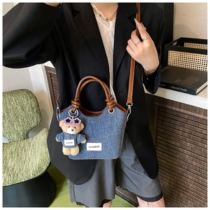 Détail du sac seau en denim avec garniture en cuir marron et pendentif ours en peluche