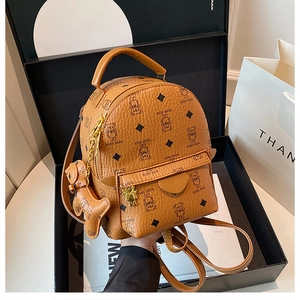 Detail of a brown leather mini backpack with bear print and matching bear charm in gift box