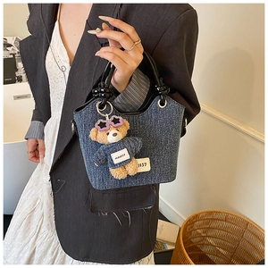 Détail du sac seau en denim avec poignées rondes et un charmant ours bleu en peluche
