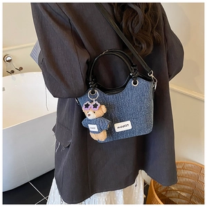 Détail du sac seau en denim bleu avec breloque ours en peluche et anses en similicuir