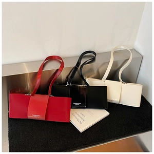 Three leather underarm bags in red, black, and white on a modern display stand
