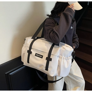Grand sac de voyage crème porté à l'épaule dans un décor intérieur de style