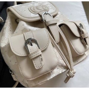 Detail of cream backpack showing silver buckles, drawstring closure and bow applique