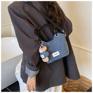 Détail du sac seau en denim avec poignée en cuir noir et charm ours mignon