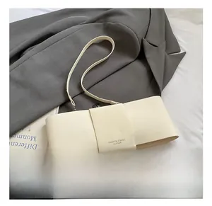 Detail of white leather underarm bag featuring a trendy wide-strap bow design and text