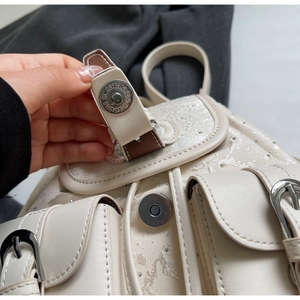 Detail of silver magnetic buckle and buckle strap on mini off-white leather backpack