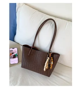 Detail of dark brown woven tote bag with colorful beaded charm and slim shoulder straps